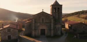 산티아고 순례길 마을의 오래된 로마네스크 양식 석조 교회. 종탑과 작은 집들이 어우러져 중세 시대의 역사적 분위기를 자아냄.